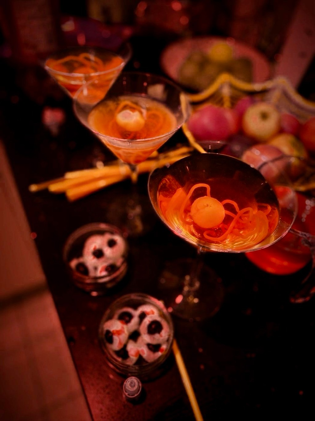 Orange cocktails in martini glasses with jelly eyeballs and sweet worms, beside bowls of eyeball sweets
