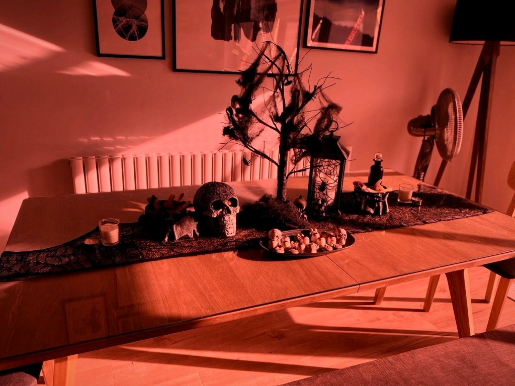 A dining table dressed with black lace, a skull, a spooky tree, a lantern and a plate of skull-shaped treats